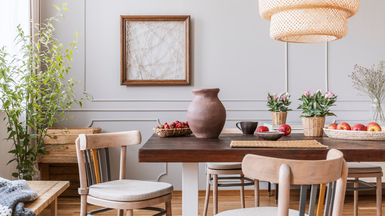 Vintage wooden chairs in living room with long table with strawberries, apples, vase and flowers on it,