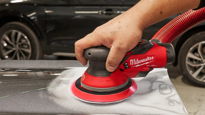 A person sanding a car with Milwaukee's M12 6-inch Random Orbital Sander