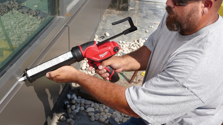 A person sealing the outside of a window frame with Milwaukee's M12 Adhesive and Caulk Gun