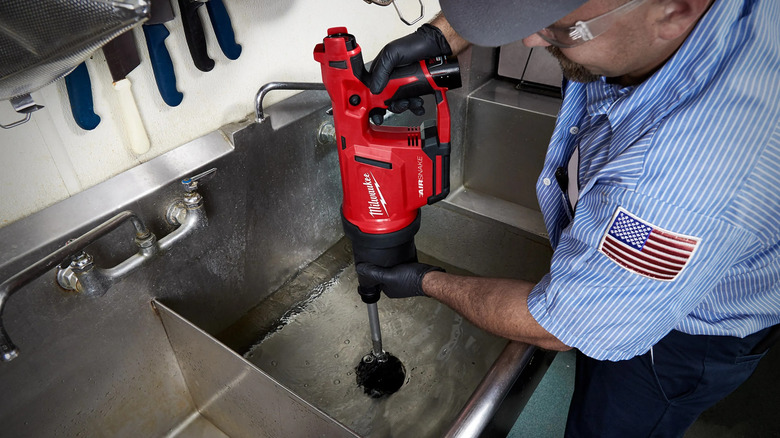 A person clearing a blocked kitchen sink with Milwaukee's M12 Drain Cleaning Airsnake