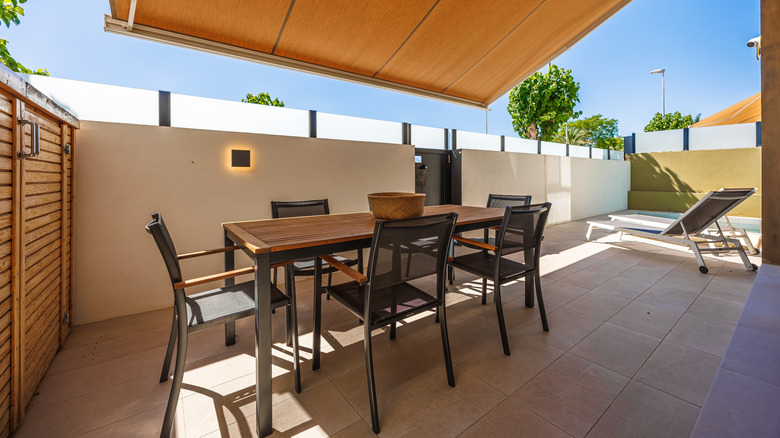 An outdoor terrace shaded by both an awning and a high wall