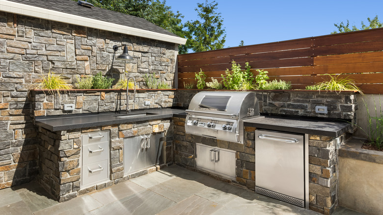 A well-equipped outdoor kitchen, with a grill, sink, faucet, and under-counter appliances