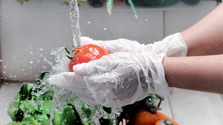 A person prepping food under a running faucet