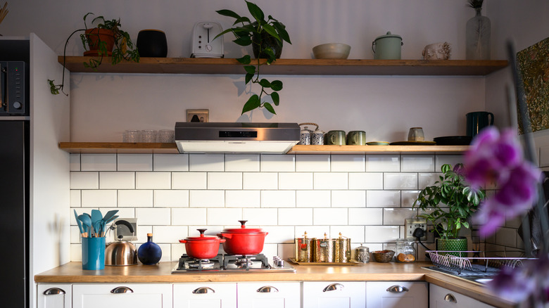 A kitchen with lots of open shelving on a white-tiled wall