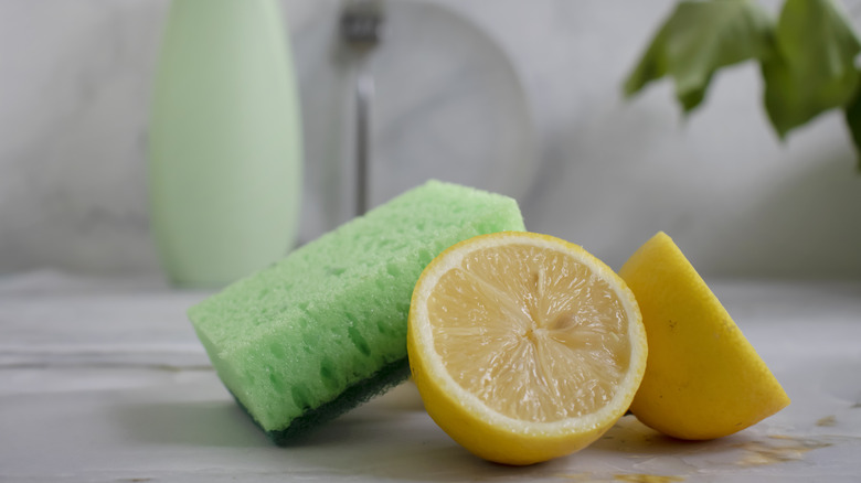 A full lemon and half a lemon beside sponge on counter