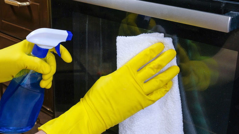 Yellow gloved hands cleaning a glass oven door