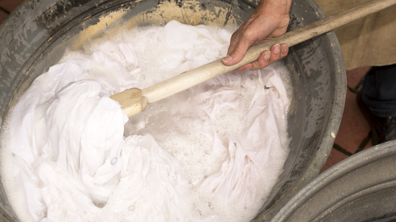 Person washing laundry with wooden laundry paddle in a metal washtub