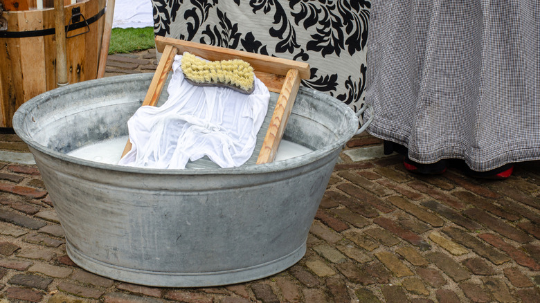 Metal washtub filled with water, washboard and brush