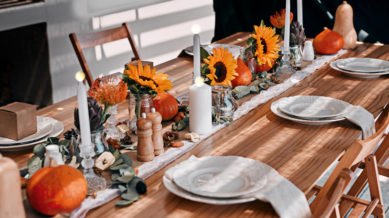 A wood table decorated with white plates and sunflowers