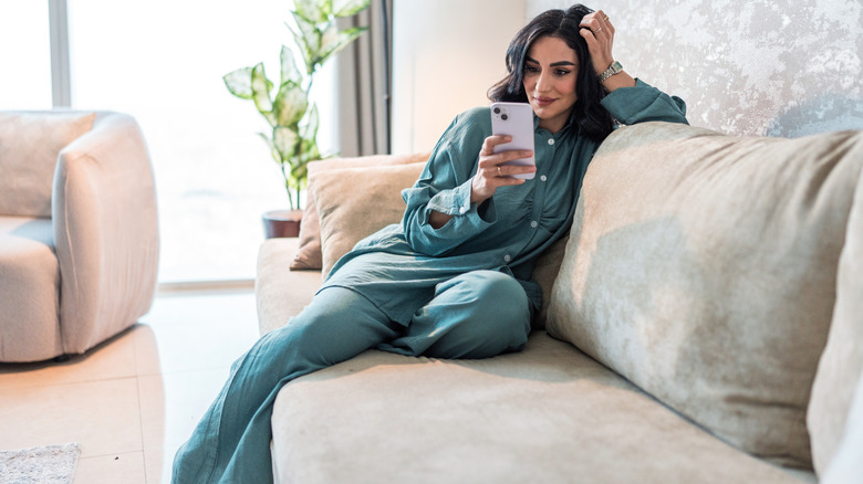 Smiling person sitting on couch while looking at smartphone