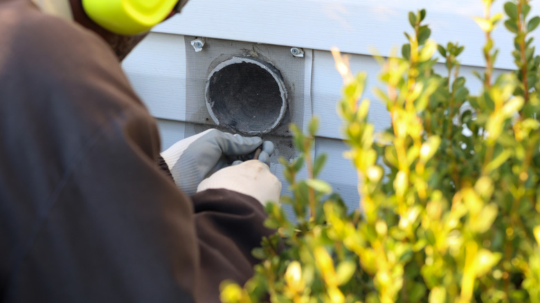 A man replacing the cover on an exterior dryer vent