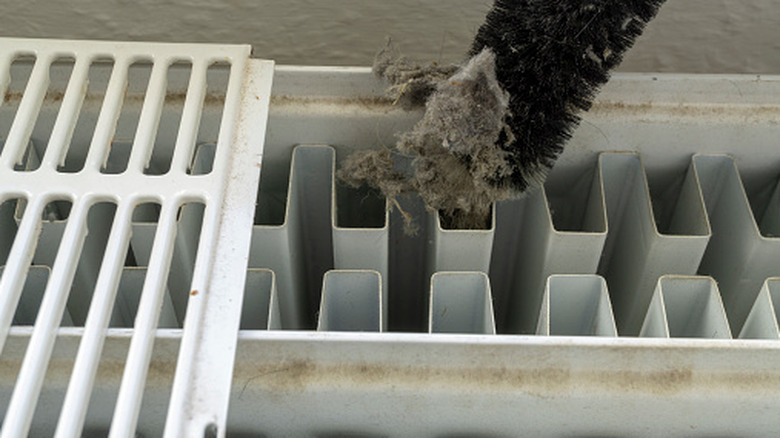 A person removing dust from a radiator with a brush