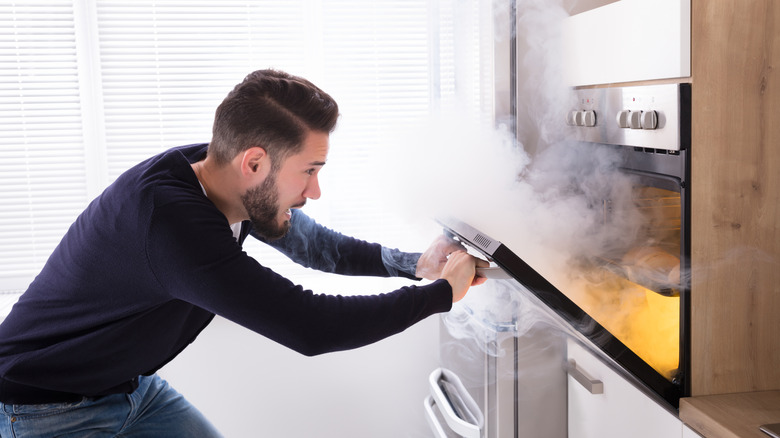 A man opening a smoky oven