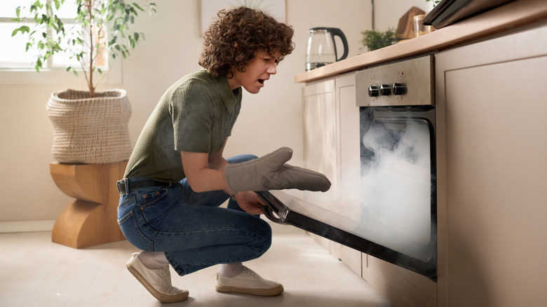 A person opening a the door to a smoking oven