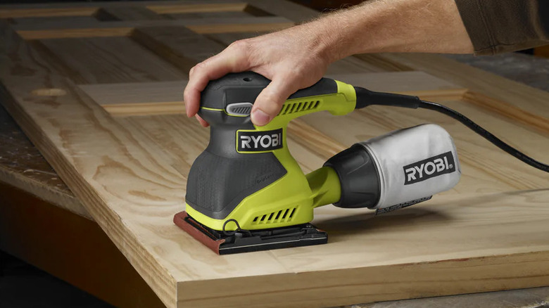 A person using Ryobi's ¼-Sheet Finish Sander on a wooden door