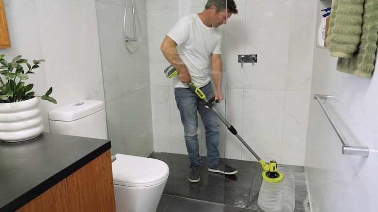 A person cleaning their bathroom with a Ryobi telescoping scrubber tool
