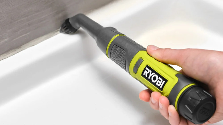 Person cleaning shower tray grout with Ryobi's lithium cordless compact detail scrubber