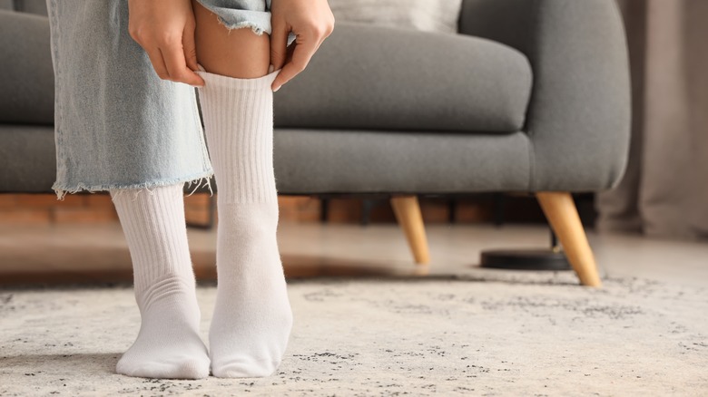 A person putting calf-high white socks on their feet