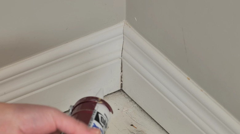 Hands pointing a caulking gun to a cracked joint in the baseboard.