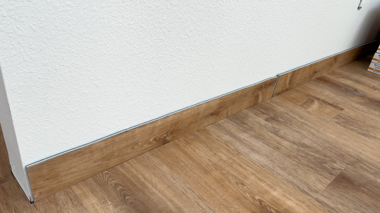 A floorboard plank being used as baseboards on a wall.