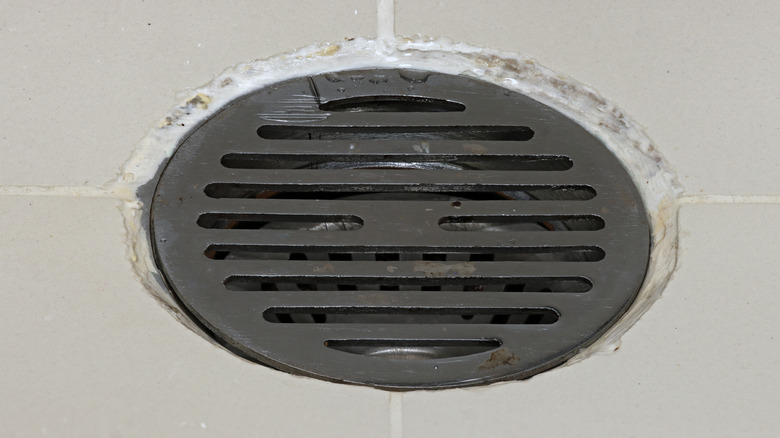 A close up of a grey drain with cream tiles