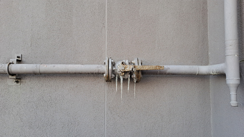 A grey pipe with icicles against a grey wall