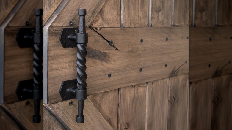 An elegant black wrought iron closet door handle installed on a wooden barn door is shown in a detail shot