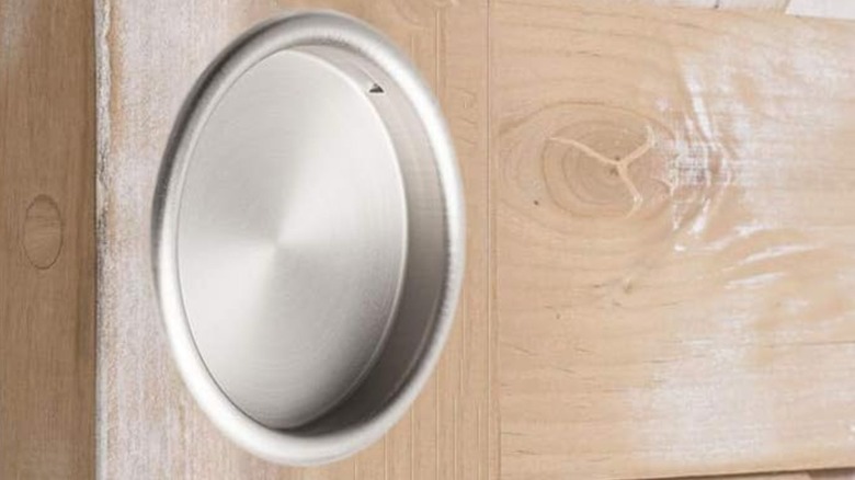 A brushed nickel closet door finger pull installed on a wood door is shown in a detail shot