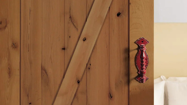A bold red closet door handle is installed on a pine wood barn door