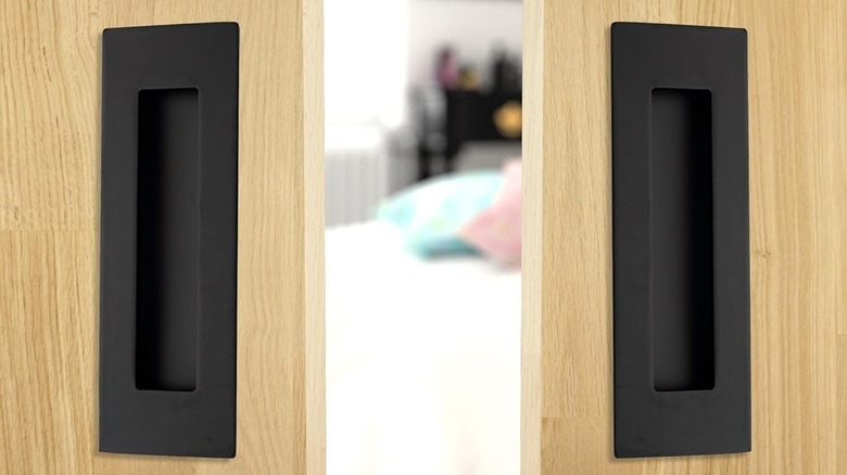 Two black recessed closet door handles are installed on light wooden doors