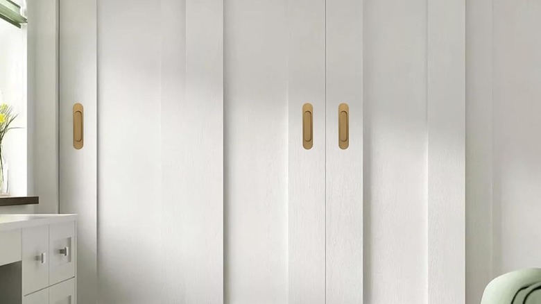 Three self-adhesive brush brass door handles are installed on white closet doors