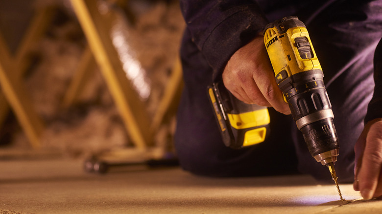 Close-up of a person working in a loft space with a black and yellow power tool