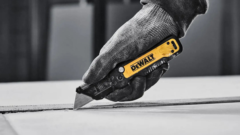 A person cutting material with DeWalt's Push and Flip Folding Lock-Back Utility Knife