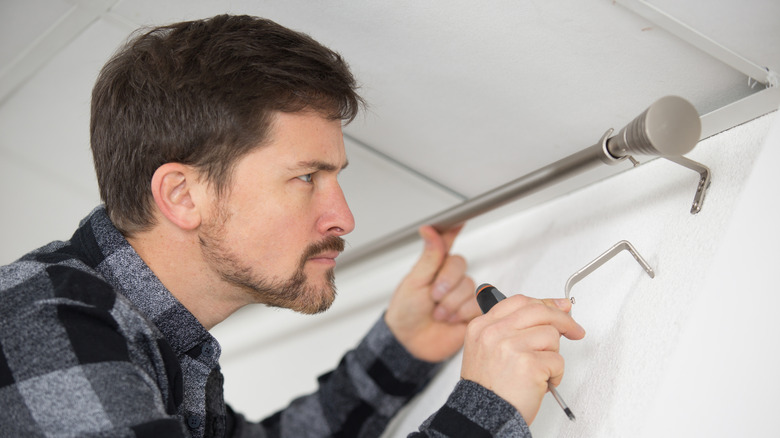 A person installing a curtain pole