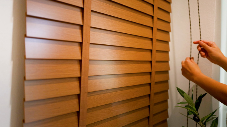 Close-up of a person pulling the cord on a set of wooden blinds