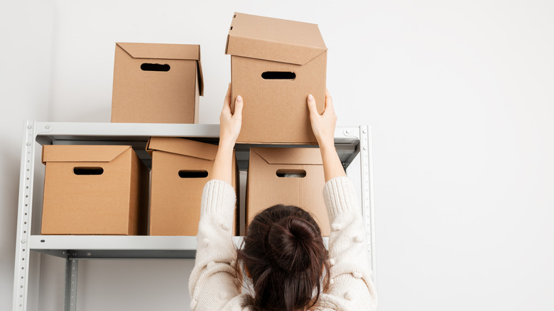 A woman placing a cardboard box on a set of metal shelves