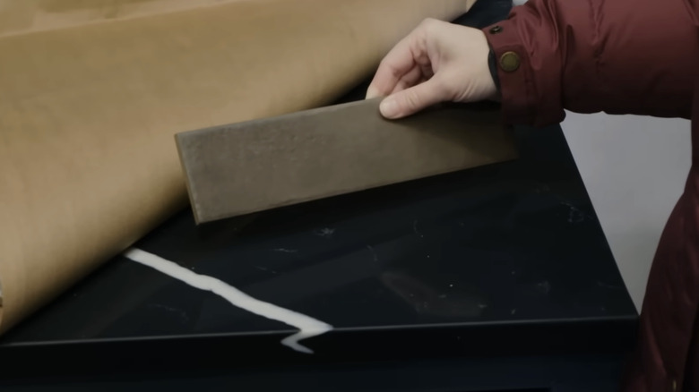 A hand holding a brown tile against a black countertop