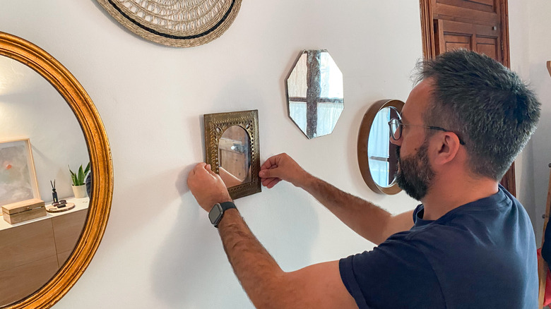 A person hanging mirrors on a gallery or collage wall in a home entryway