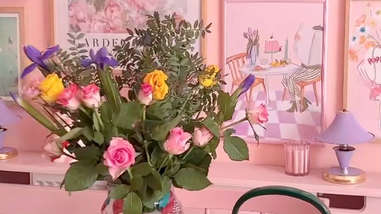 Room with pink walls, pink framed art, and vase of flowers