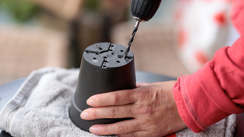 A woman holds a plastic flower pot while drilling holes to improve drainage.
