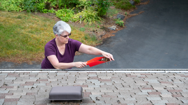 A person cleaning their gutters with a red gutter scoop