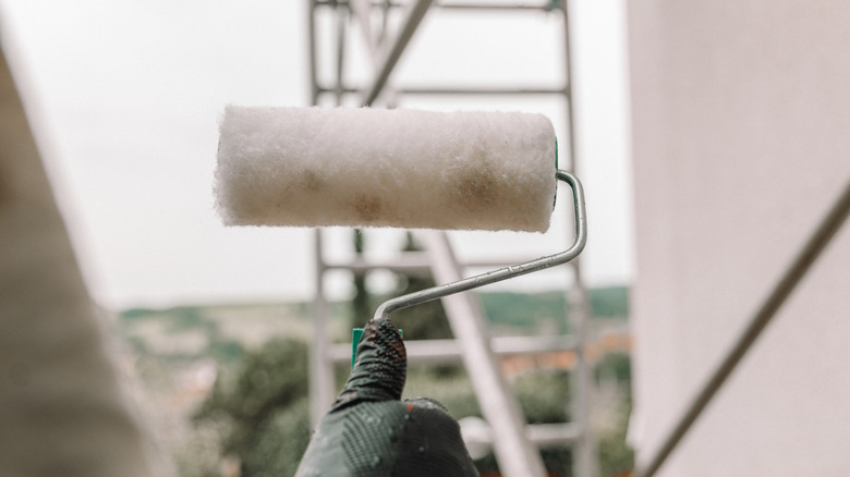 A person holding a paint roller with a ladder in the background