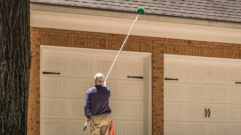 A person cleaning gutters with a telescoping brush