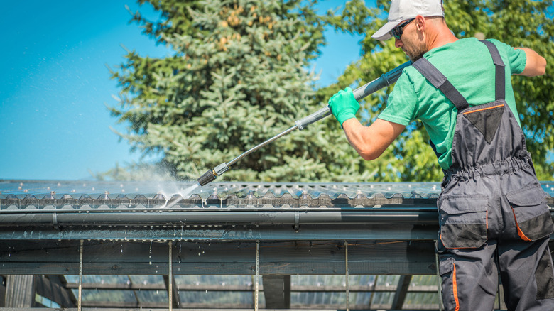 A worker cleaning gutters with a pressure washer