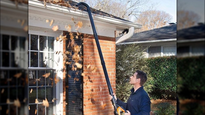 A person using a leaf blower with an extension kit to clean their gutters