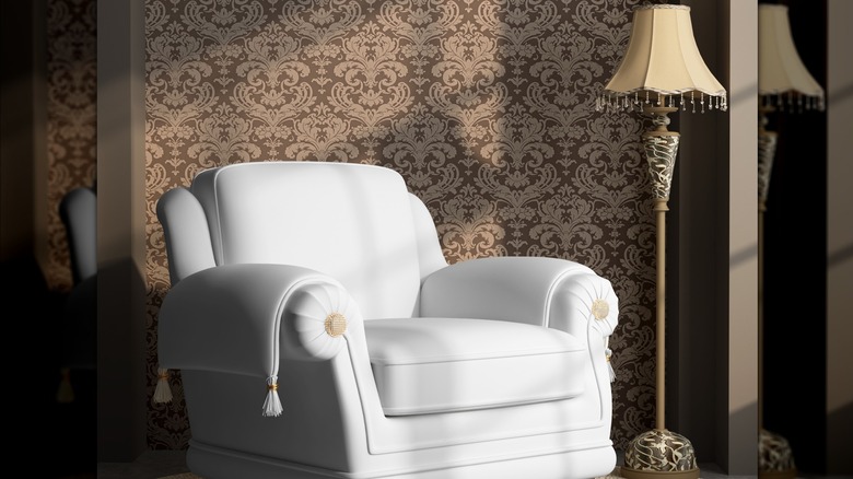 A light armchair sitting in front of a brown and cream damask patterned wall.
