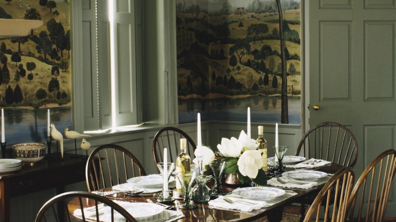 A dining room with an antique dining set and pastoral wallpaper on the walls.