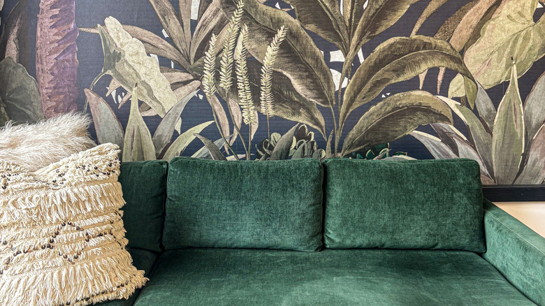 Botanically themed wallpaper behind a green velvet couch.