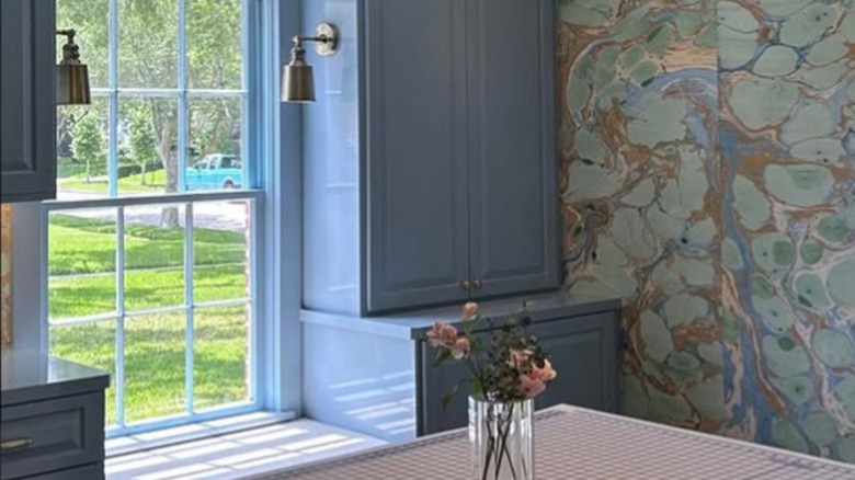 A kitchen space with blue cabinets and marbled wallpaper.