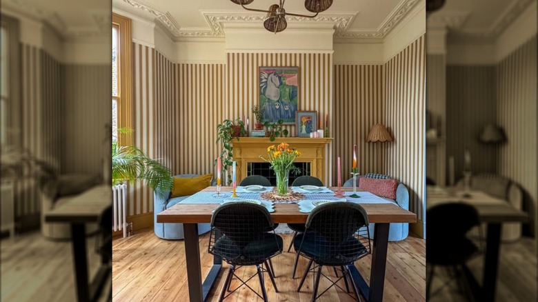 A dining room with ticking stripe wallpaper, crown molding, and a painted fireplace.